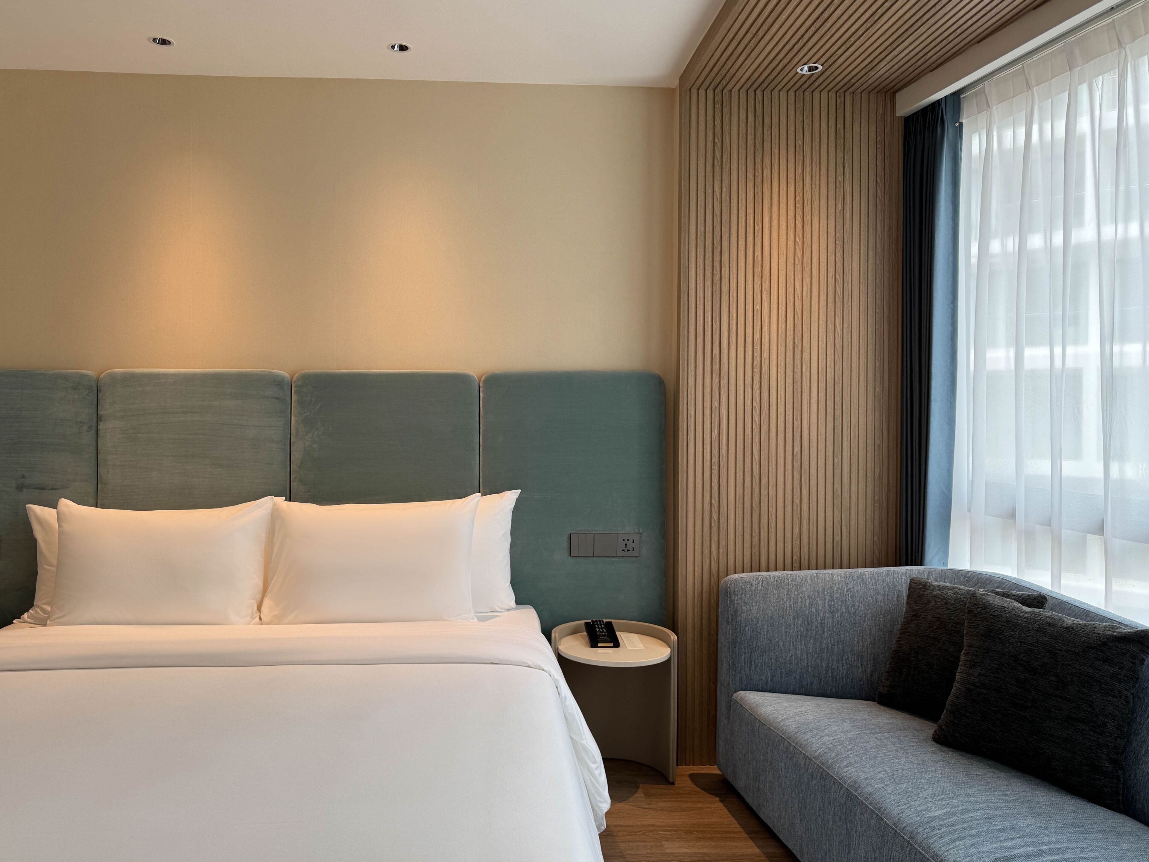 Una habitación de hotel con una cama, una mesita de noche con un control remoto y un sofá.