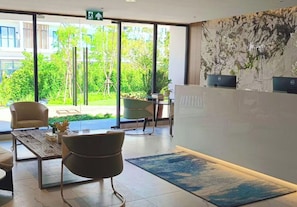 A reception area with a desk, chairs, a coffee table, and a view of greenery outside.