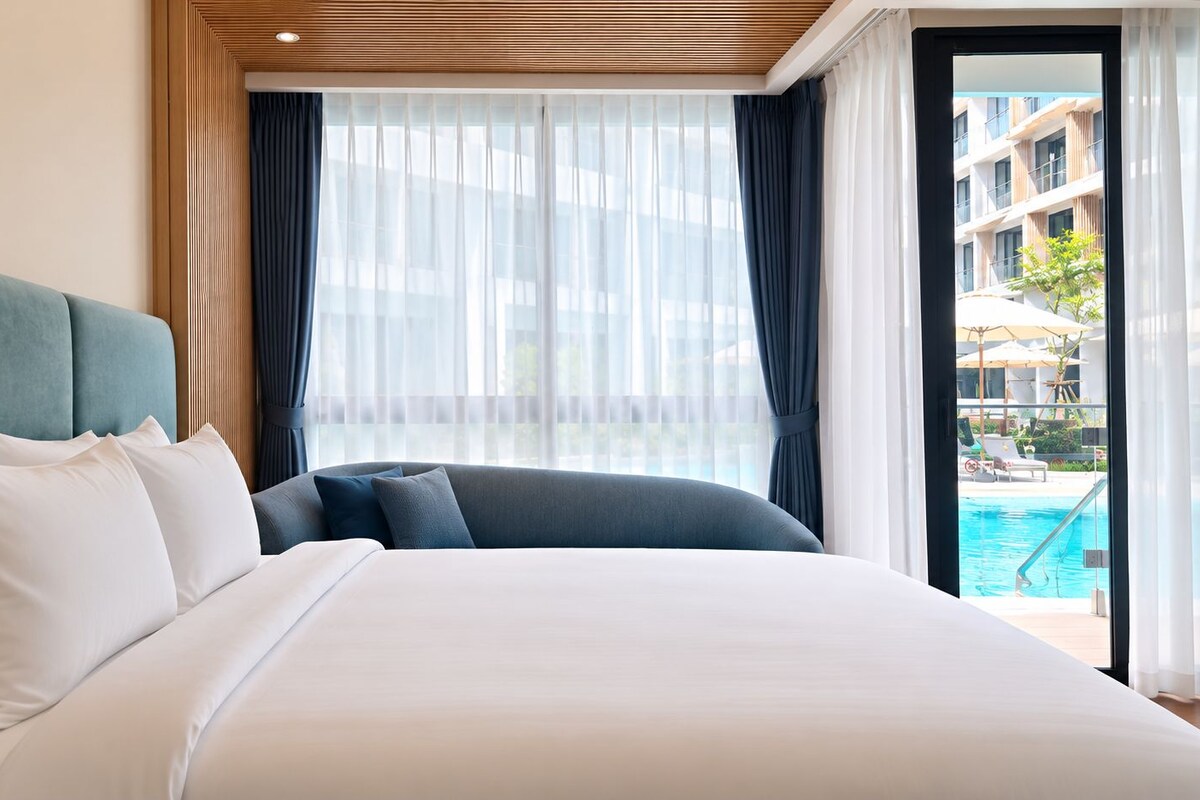 A hotel room with a large bed, a view of a swimming pool, and a balcony.