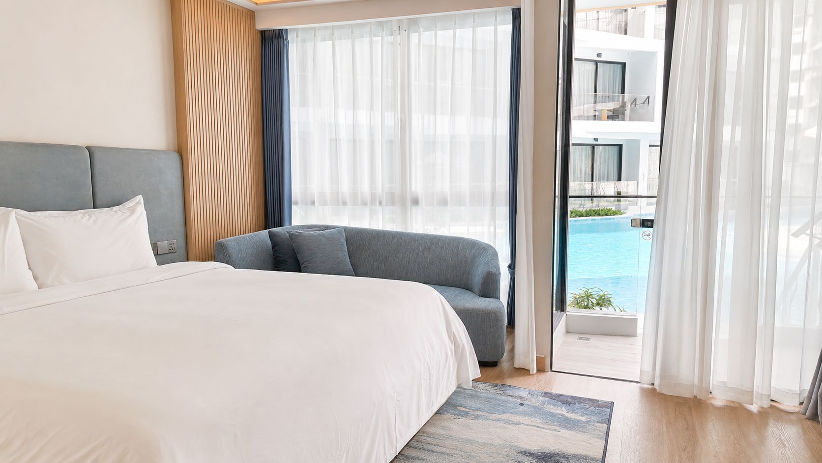 Habitación de hotel con una cama, un sofá gris y vistas a una piscina.