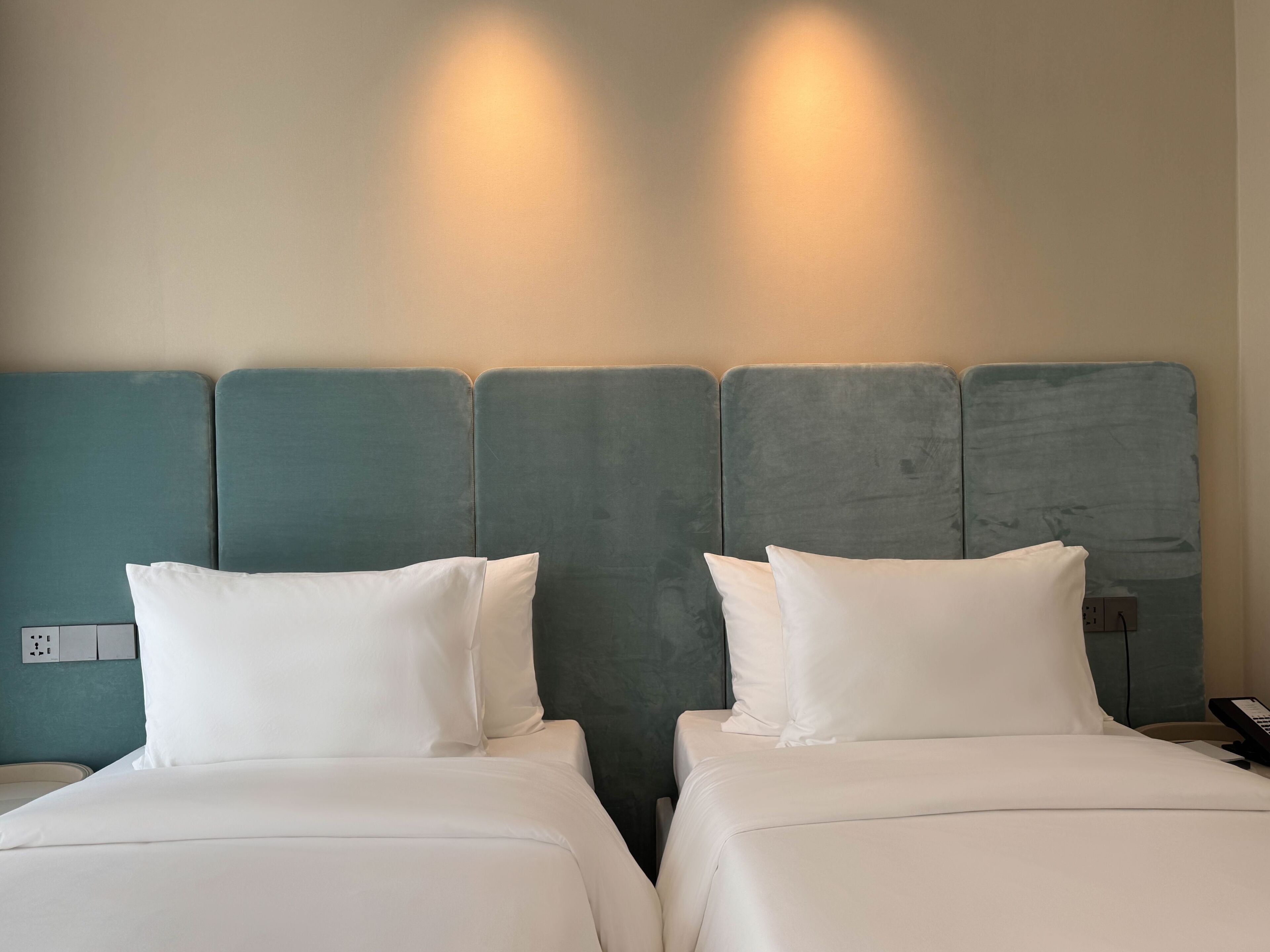 A hotel room with two beds, each with white bedding and pillows, and a teal headboard.