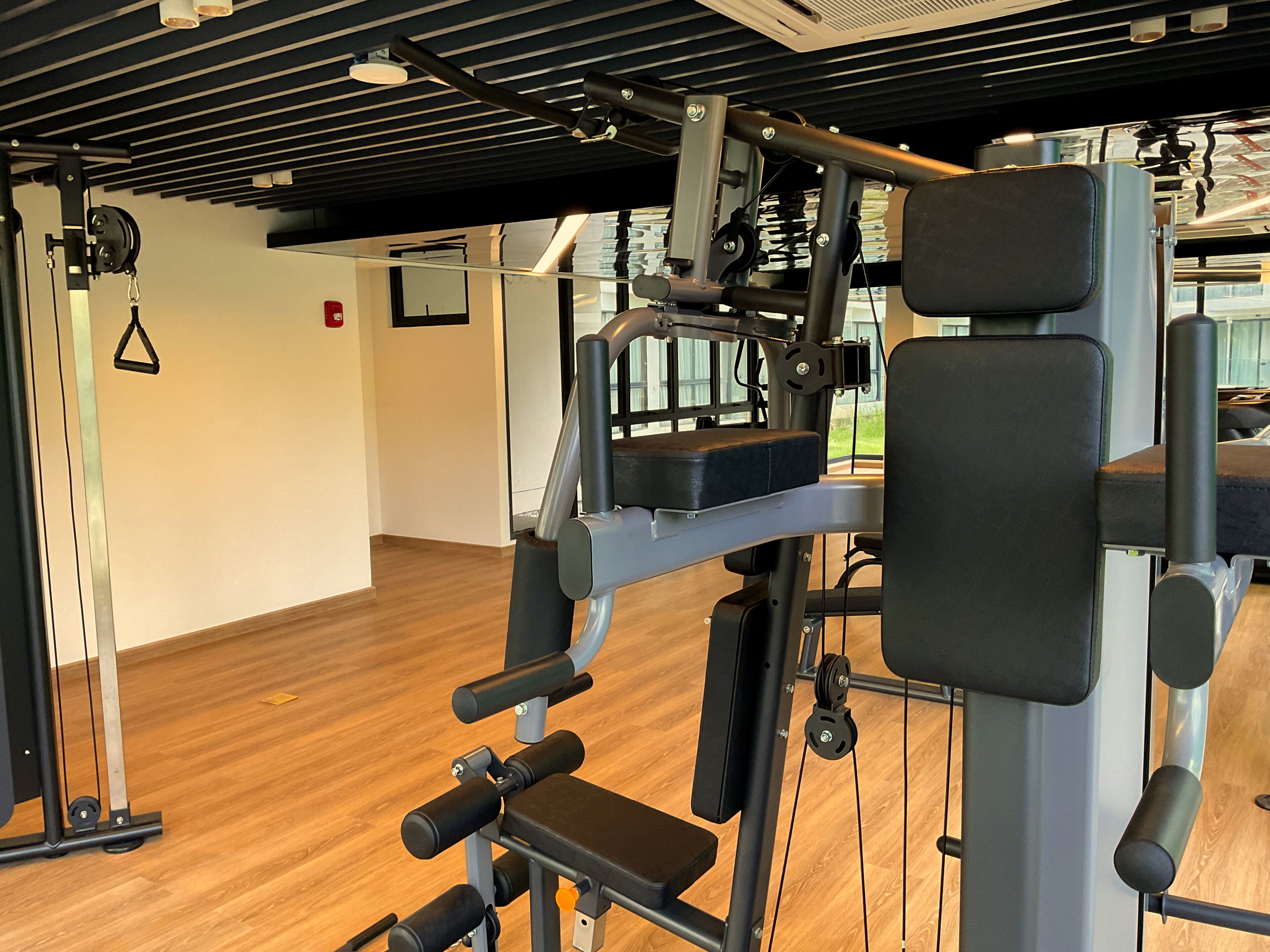 A gym with exercise equipment, wooden flooring, and a ceiling with linear lights.
