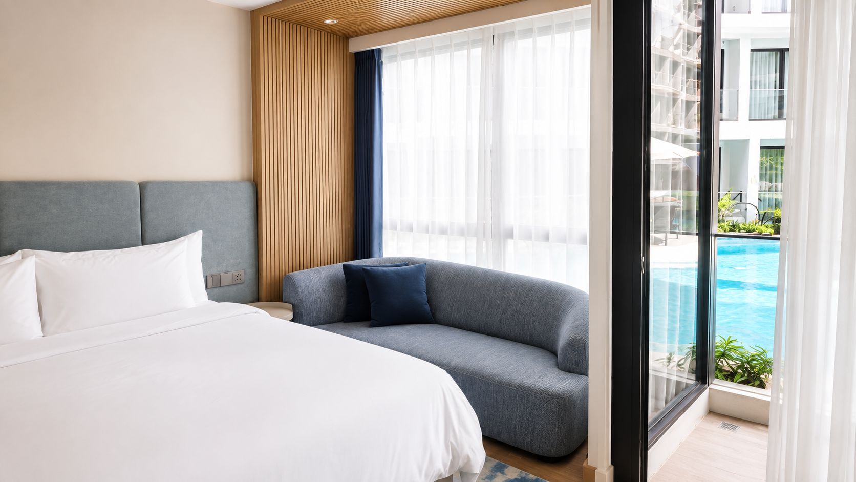Habitación de hotel con cama, sofá y ventana con vista a una piscina.