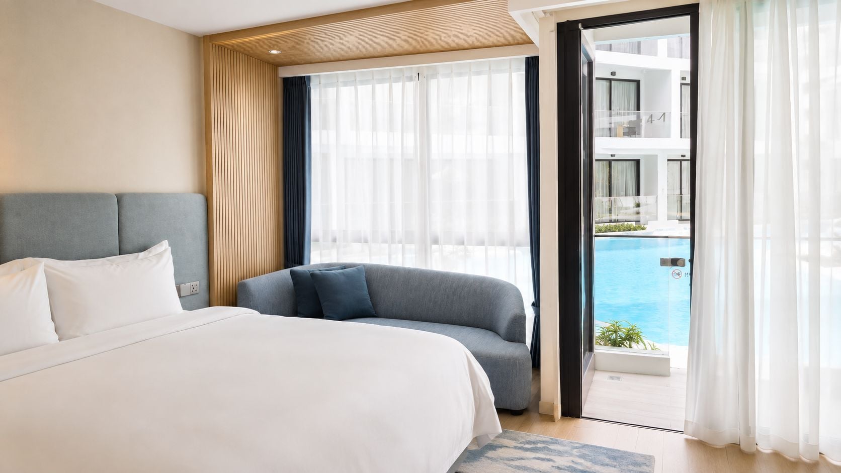 Habitación de hotel con cama, sofá, ventana grande y vista a una piscina.