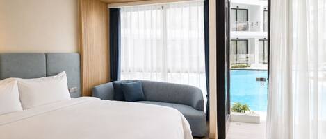 Habitación de hotel con cama, sofá, ventana grande y vista a una piscina.