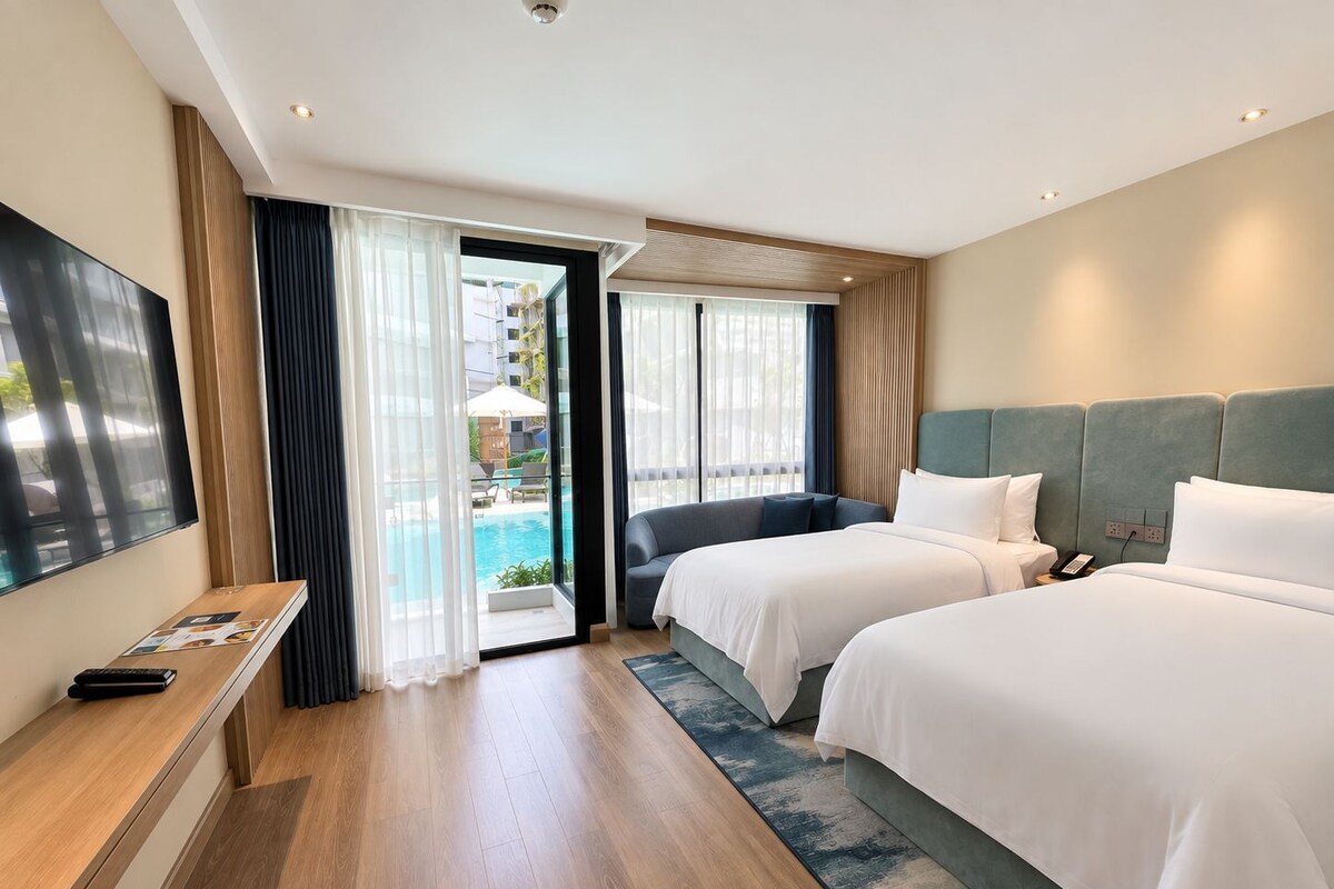 A hotel room with two beds, a TV, and a view of a swimming pool.