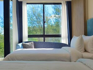 A hotel room with a large window, a bed, and a view of trees. - Laya Suites & Residences (Choeng Thale)