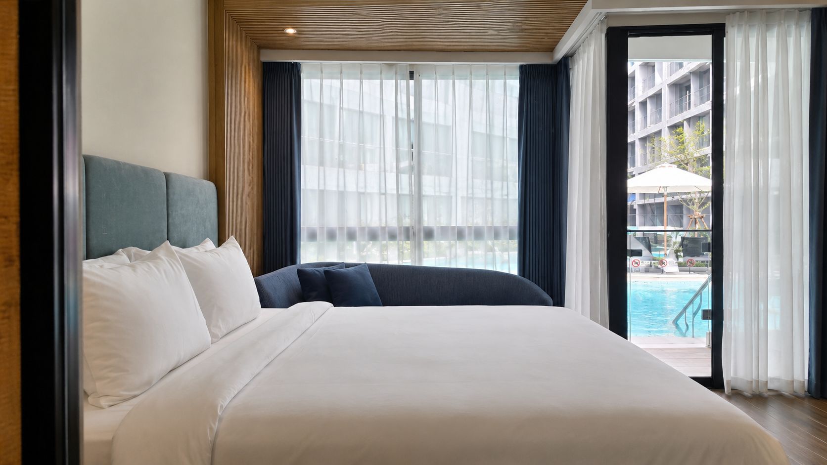 A hotel room with a large bed, a view of a swimming pool, and a balcony.