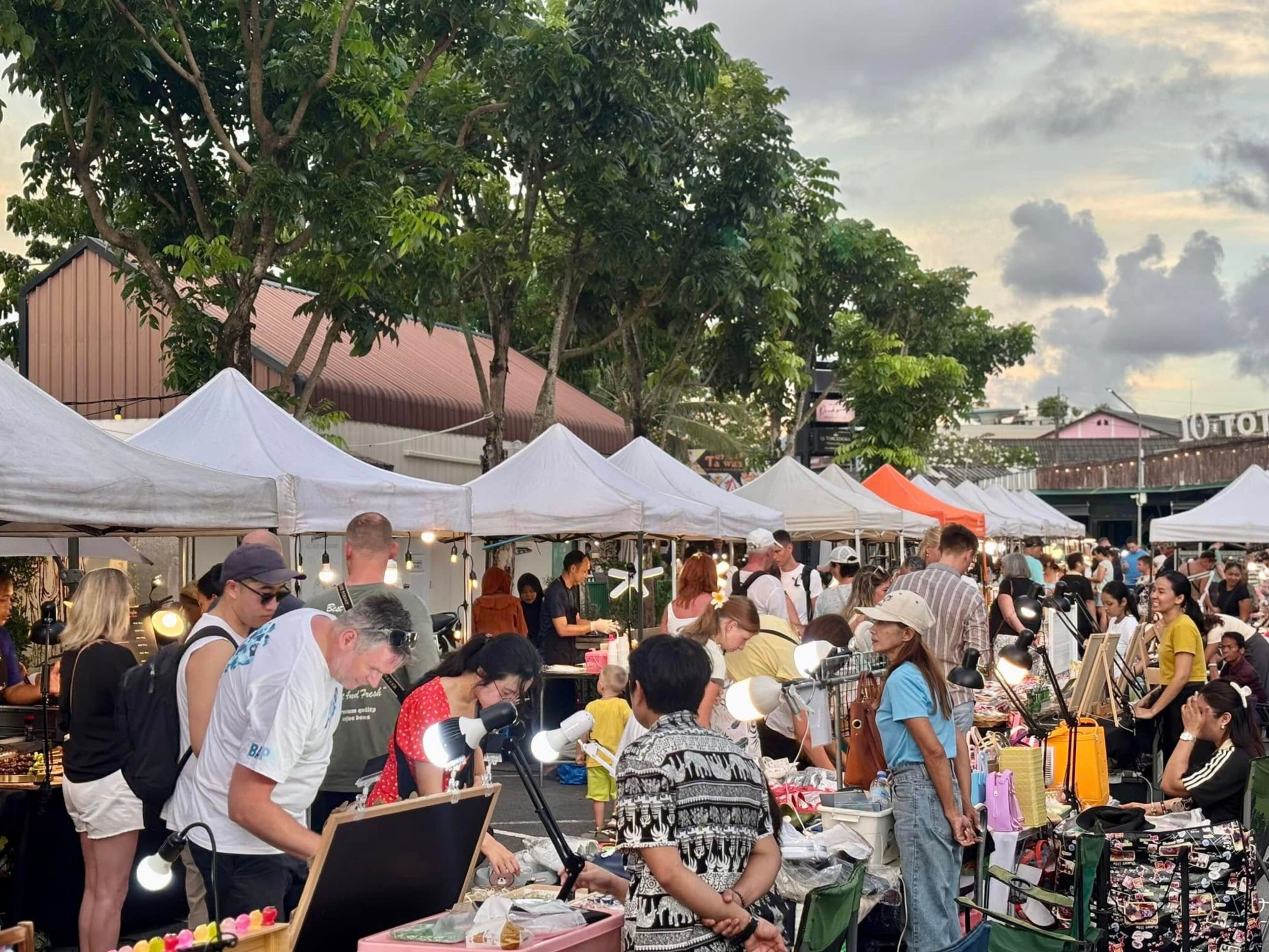 A crowded outdoor market with white tents and people browsing stalls.