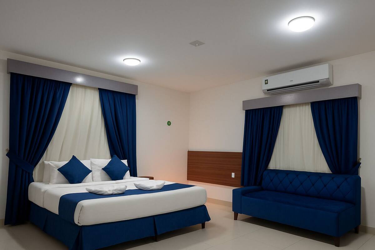 A hotel room with a bed, a sofa, and an air conditioning unit.