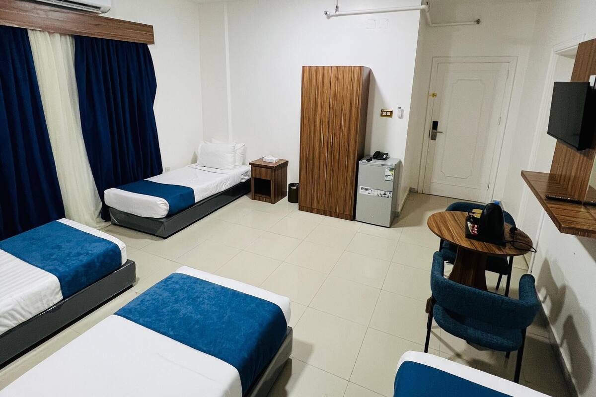 A hotel room with three beds, a desk, a chair, a wardrobe, a television, and a door.