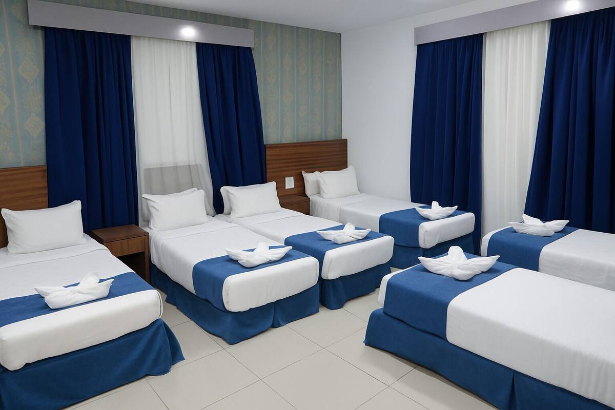 A hotel room with four beds arranged in a U-shape, each with white linens and blue bedspreads.