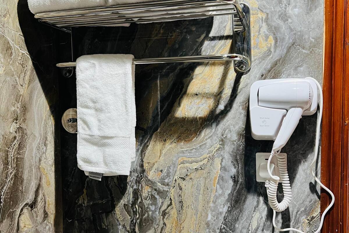 A bathroom with a marble wall, a towel rack with a folded towel, and a hairdryer plugged in.