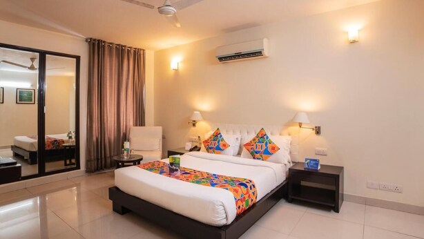 A hotel room with a large bed, two bedside tables, a ceiling fan, an air conditioning unit, and a sliding glass door leading to a balcony. - Hotel Diamond Tree (New Delhi)