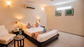 A hotel room with a bed, a chair, a small table with a bottle, and two wall-mounted lamps. - Hotel Diamond Tree (New Delhi)