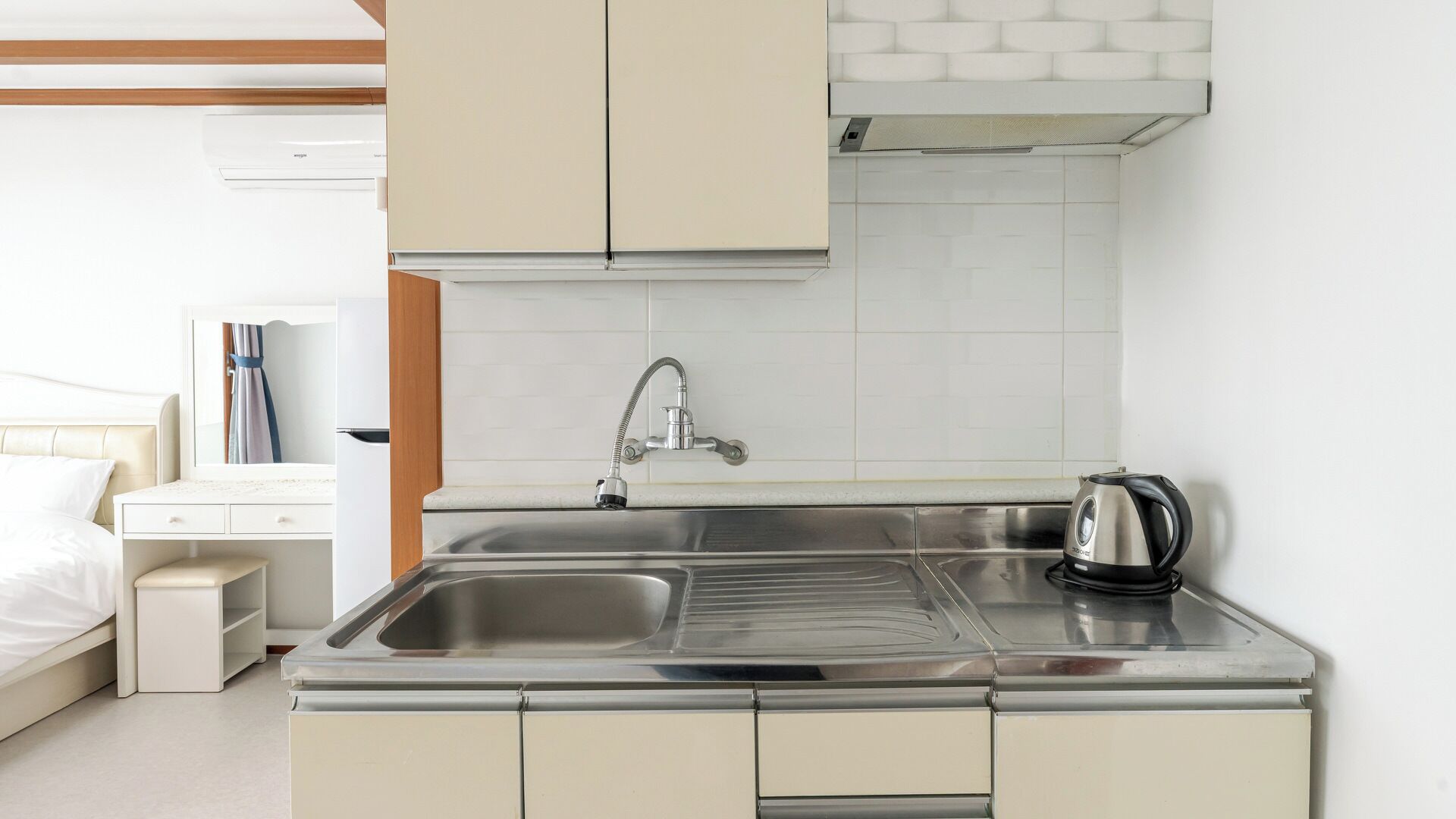 A kitchenette with a stainless steel sink, a kettle, and a cabinet.