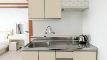 A kitchenette with a stainless steel sink, a kettle, and a cabinet.