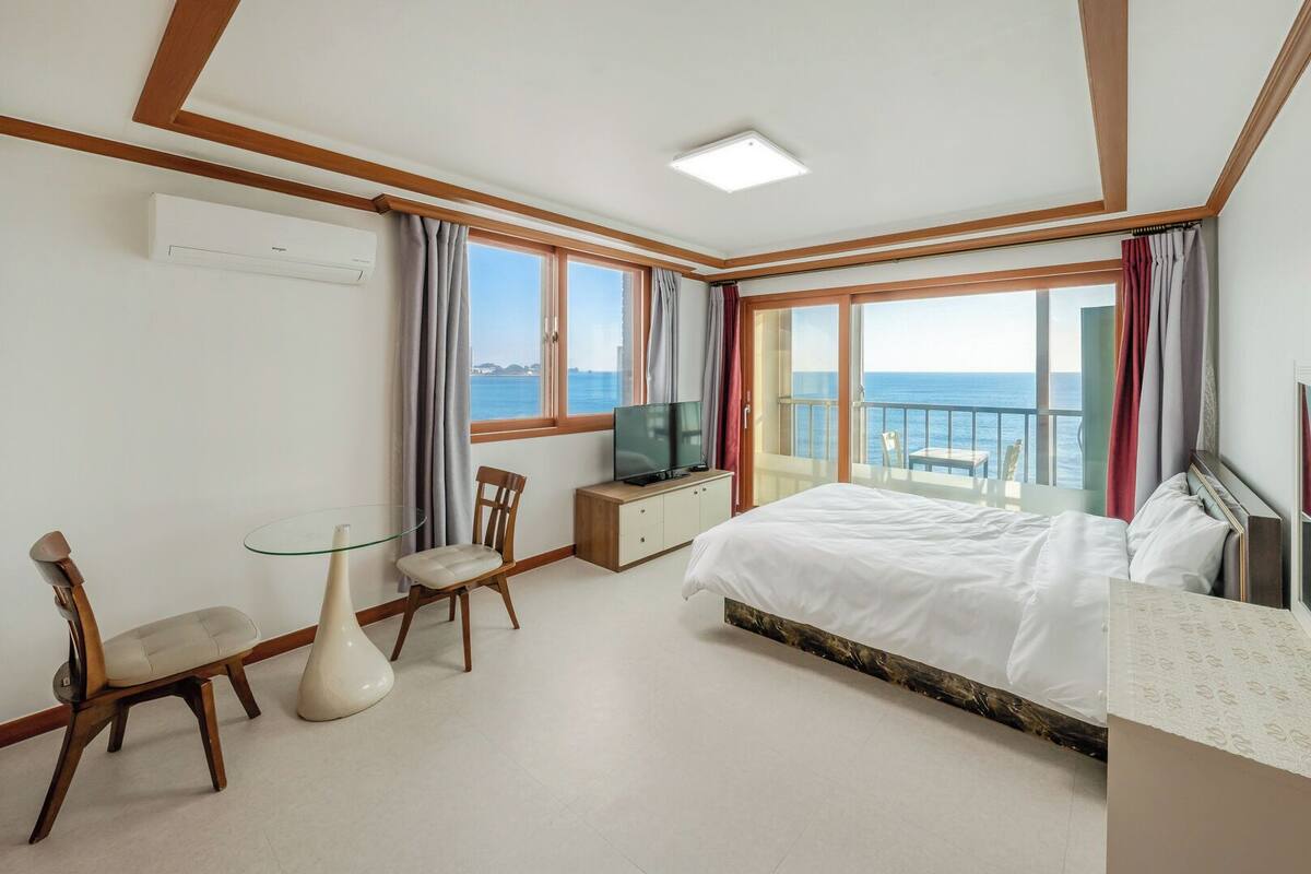Una habitación de hotel con cama, televisión, escritorio, silla y balcón con vistas al mar.
