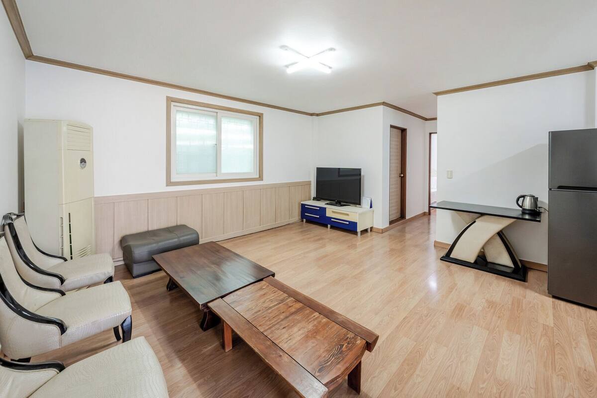 Una habitación con un banco de madera, un televisor sobre un mueble, un refrigerador y un armario.