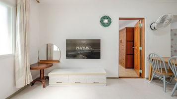 Una habitación con cama, espejo, reloj en la pared, puerta que da a otra habitación y ventilador fijado a la pared.