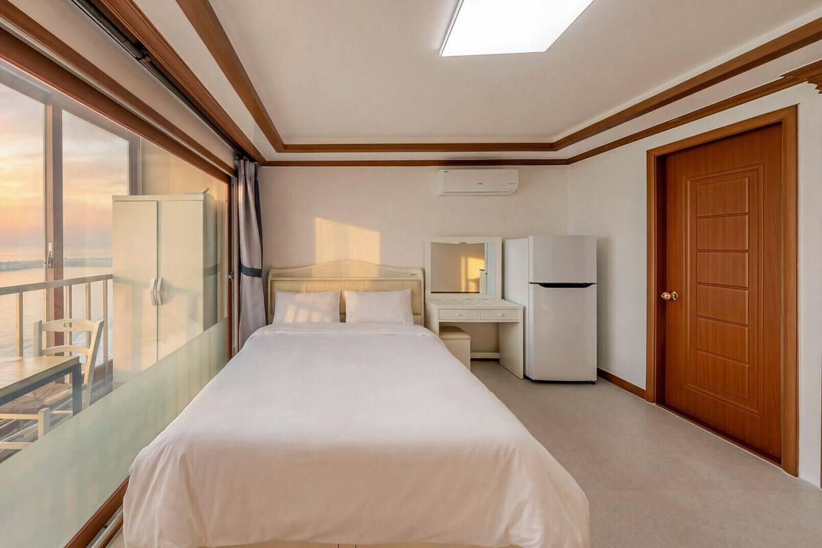 Habitación de hotel con cama, escritorio, silla, armario y vista al mar.