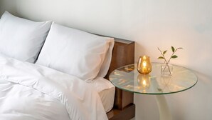 A neatly made bed with white linens, a glass table with a candle, and a small vase with a plant. - Sokcho SBS Pension (Sokcho)