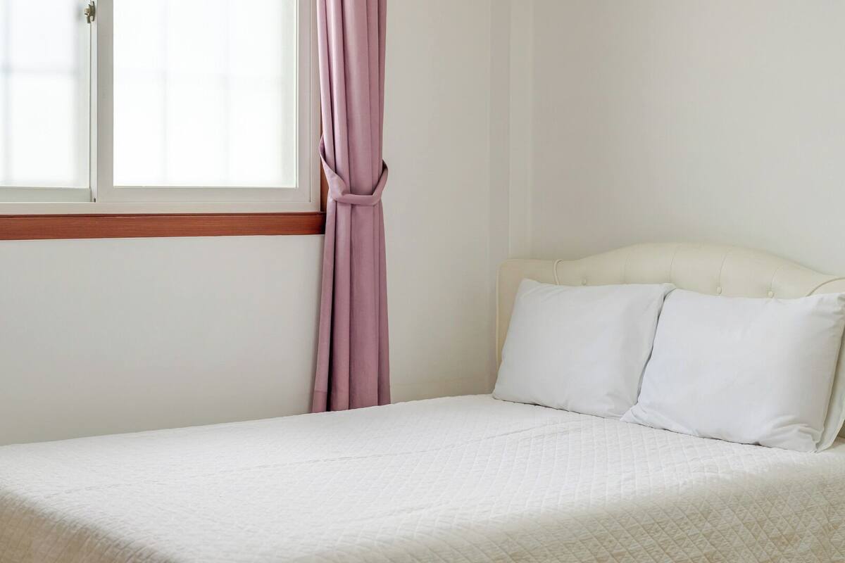 Una cama individual con colchón blanco acolchado, cabecera y dos almohadas blancas.