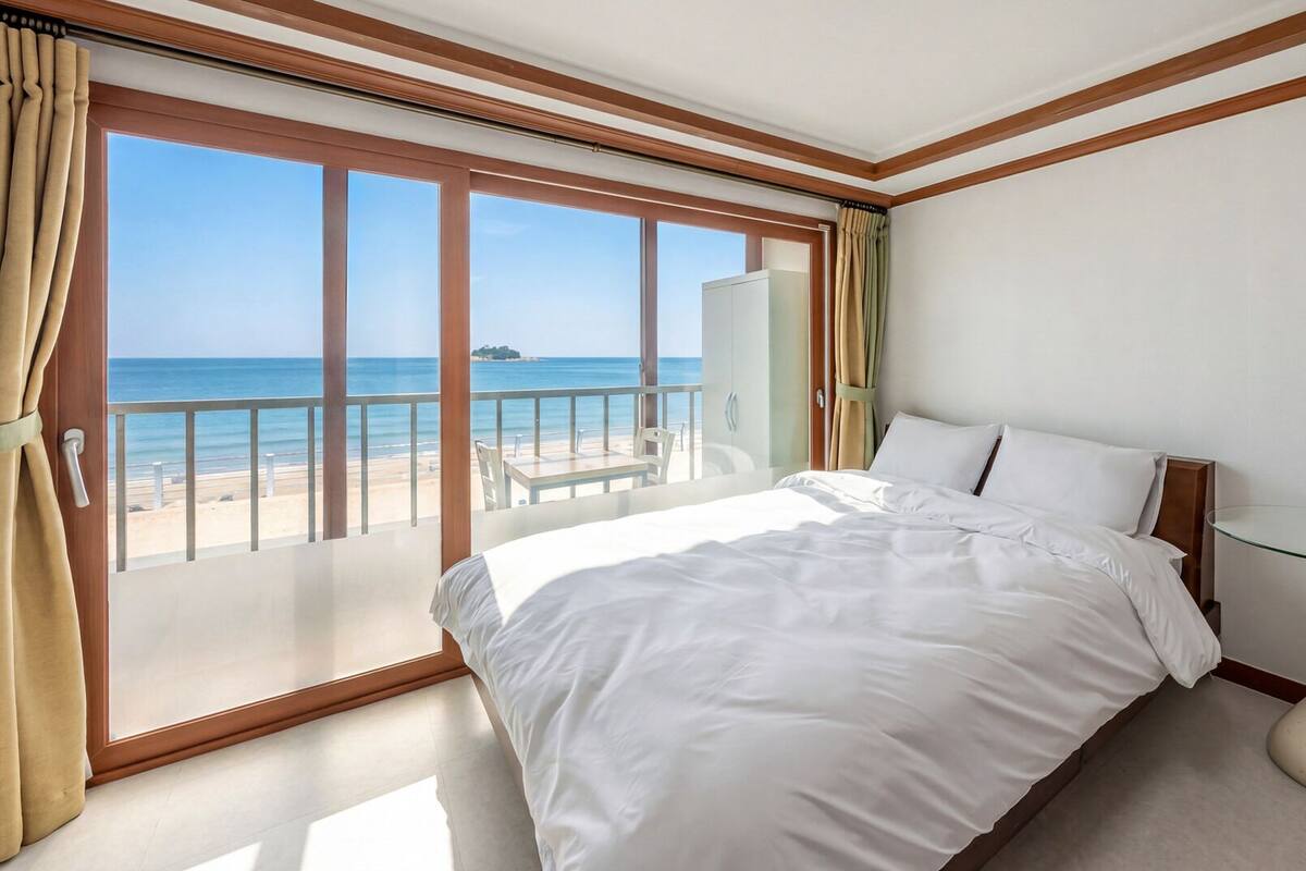 Habitación de hotel con un ventanal grande, una cama, una mesita de vidrio y vista a la playa.