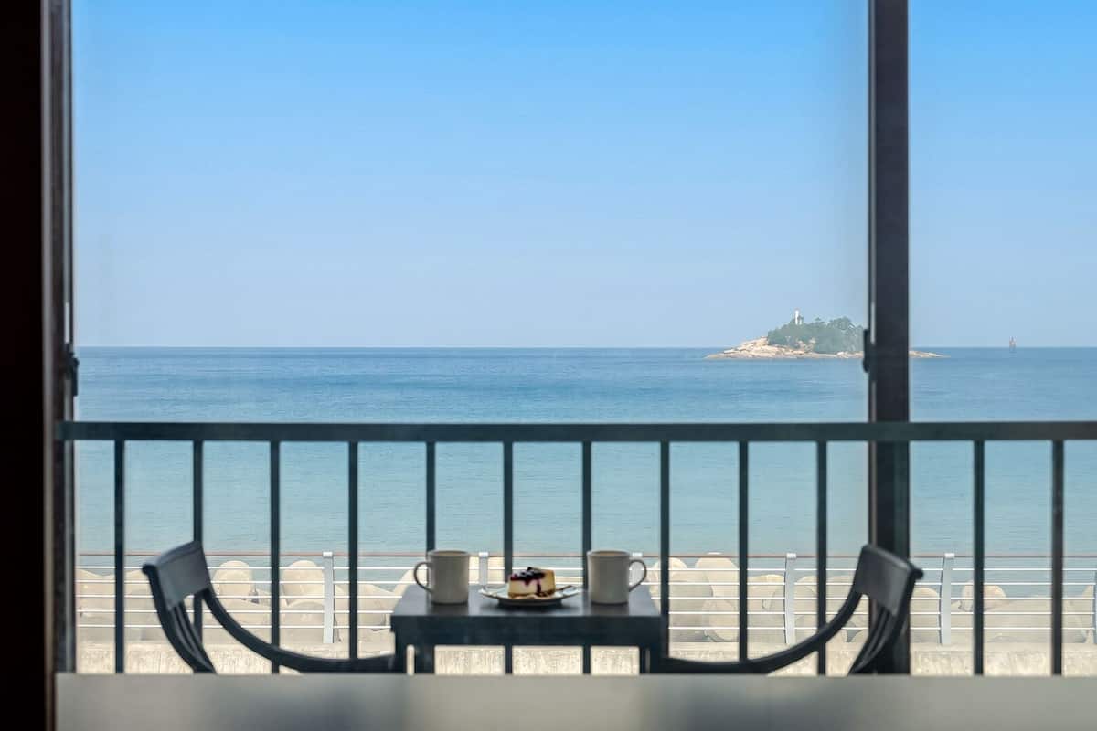 Un balcón con una mesa, dos sillas y vistas al mar y una isla distante.