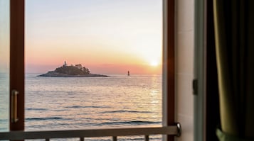 Vista del mar con un faro y una pequeña isla al atardecer.
