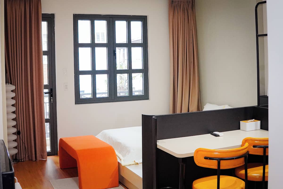 A room with a bed, a desk with chairs, a window, and curtains.