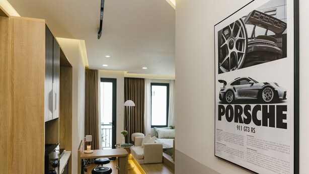 Une cuisine moderne avec un coin repas, un salon doté d’un canapé et d’une table basse, et une grande affiche d’une Porsche 911 GT3 RS accrochée au mur.