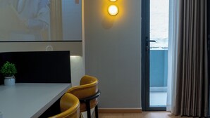 Une chambre moderne équipée d’un bureau, de deux chaises, d’une petite plante et d’une porte donnant sur un balcon.