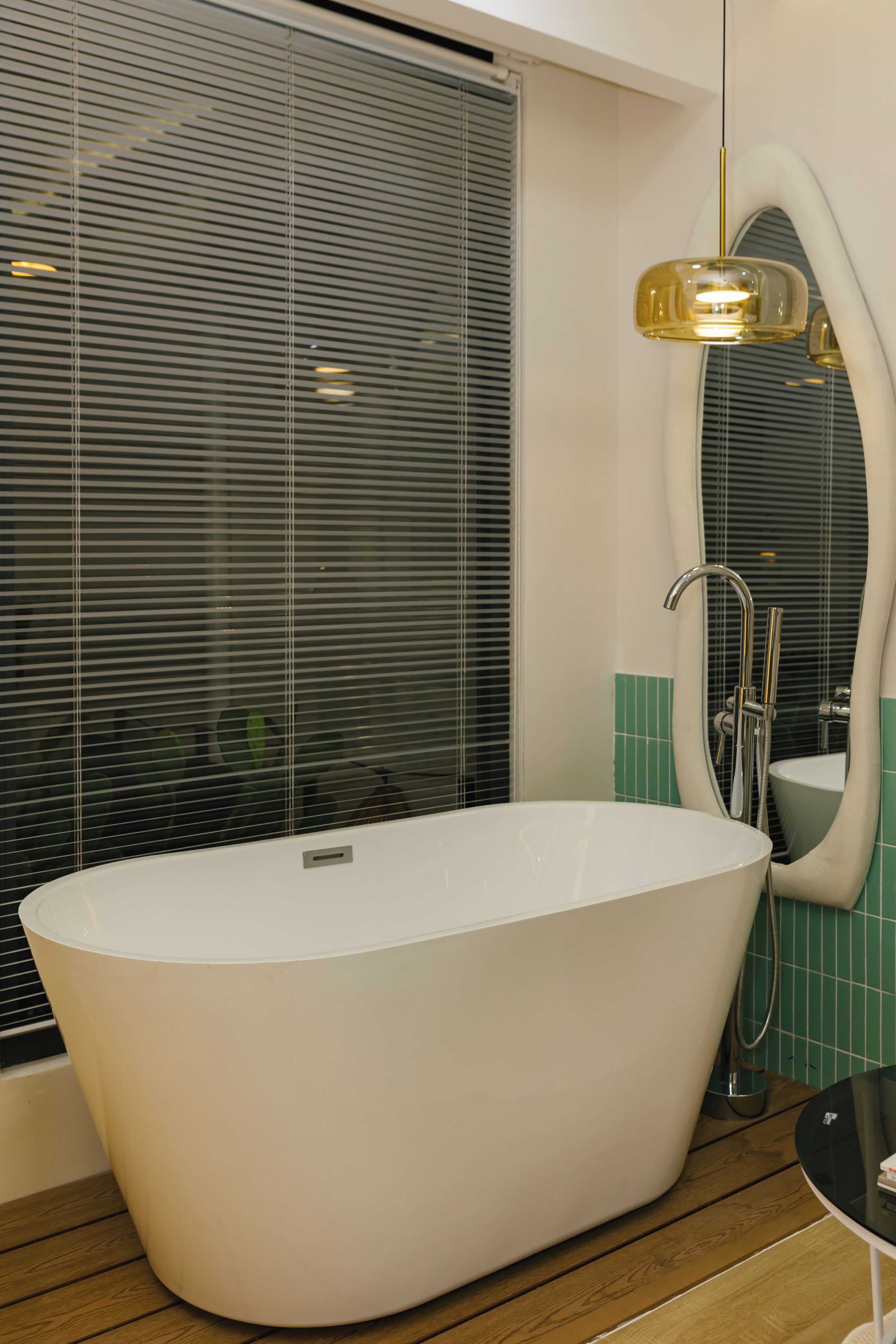 A modern bathroom with a freestanding bathtub, a vanity with a mirror, and a window with blinds.