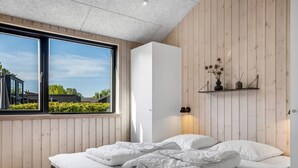 A modern bedroom with a large window, wooden walls, a bed with white bedding, and a shelf with decorative items.
