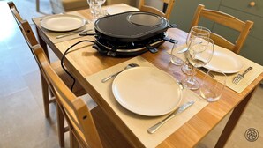 Une table à manger dressée avec des assiettes, des couverts et des verres à vin, et un barbecue portable placé au centre.