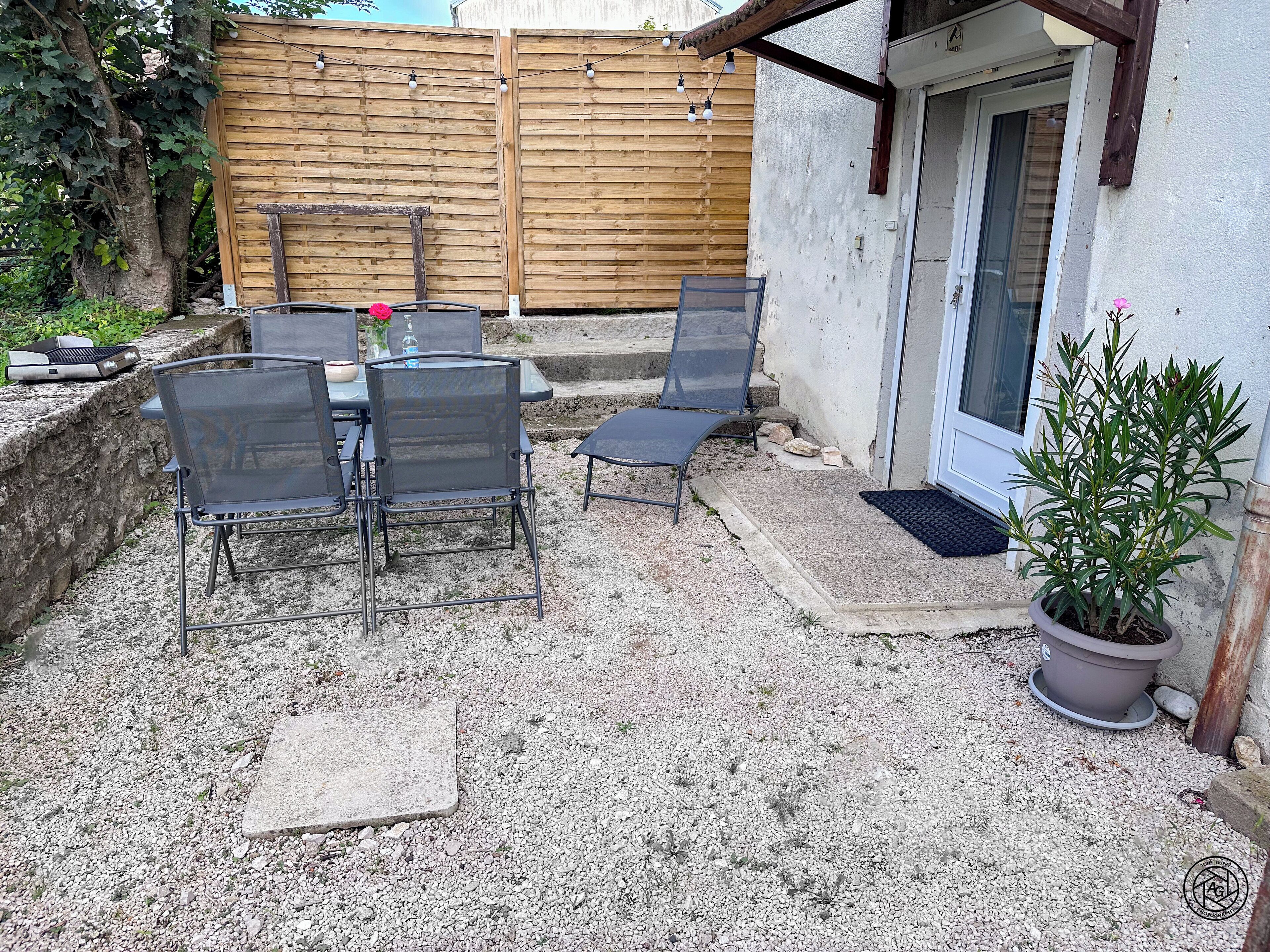 Une terrasse extérieure avec une table et des chaises, une clôture en bois et un pot de fleurs.