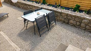 A patio with a glass table and chairs, surrounded by a stone wall and wooden fence.