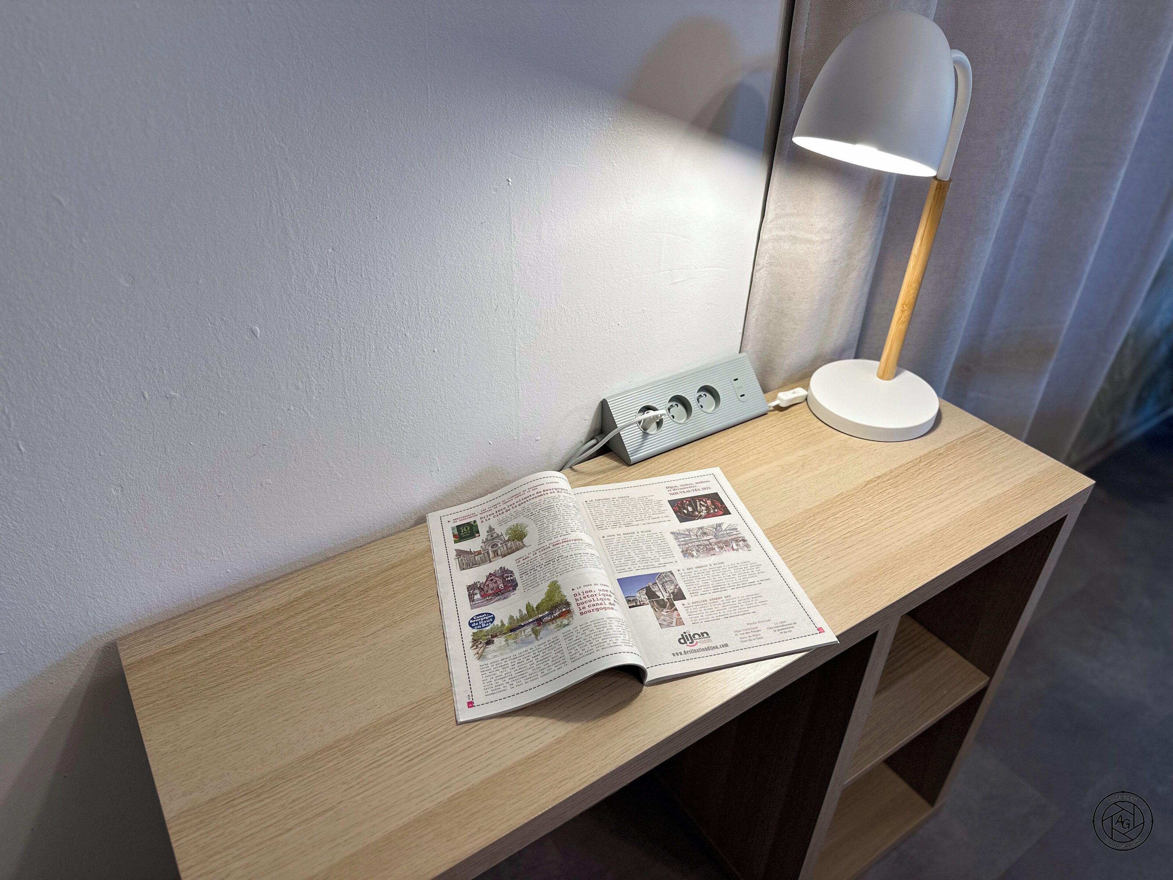 A wooden desk with a lamp, a power strip, and an open magazine.