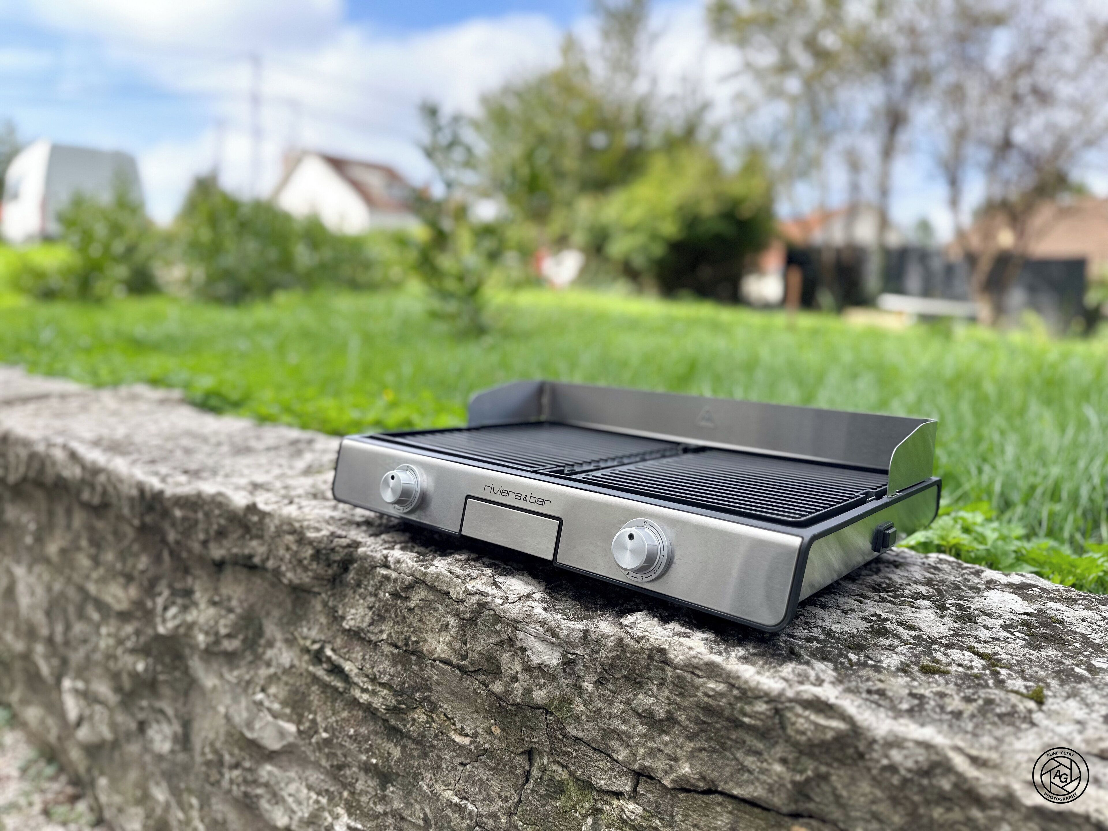 A portable grill with two knobs, placed on a stone surface outdoors.