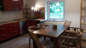 A kitchen with red cabinets, a wooden dining table, and chairs. There is a window with a view of greenery outside. - Farmhouse with large garden in the immediate vicinity of Lake Tollensesee (Blumenholz)