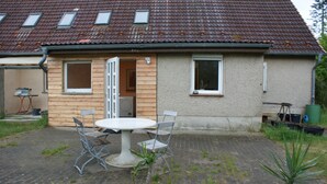 A house with a tiled roof, a wooden door, and a small patio with a table and chairs. - Farmhouse with large garden in the immediate vicinity of Lake Tollensesee (Blumenholz)