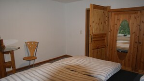 A bedroom with a bed, a wooden chair, a desk with a lamp, and a wooden door with a window. - Farmhouse with large garden in the immediate vicinity of Lake Tollensesee (Blumenholz)