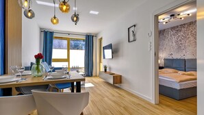 Uma sala de estar moderna com área de jantar, televisão na parede e cama com cabeceira.