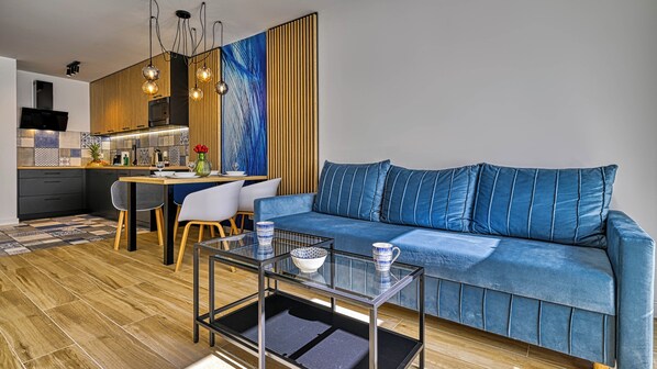 Ein modernes Wohnzimmer mit einem blauen Sofa, einem Glastisch und einem Essbereich mit Holztisch und Stühlen.