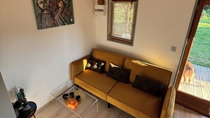 A modern living room with a yellow sofa, a painting on the wall, a window, and a view of the outdoors. - A cottage in an orchard (Conteville)
