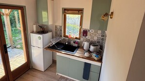 A compact kitchen with a wooden ceiling, a built-in sink, a refrigerator, and a window with a view of greenery. - A cottage in an orchard (Conteville)