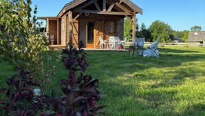 A wooden cabin with a porch, outdoor seating, and a grassy yard. - A cottage in an orchard (Conteville)