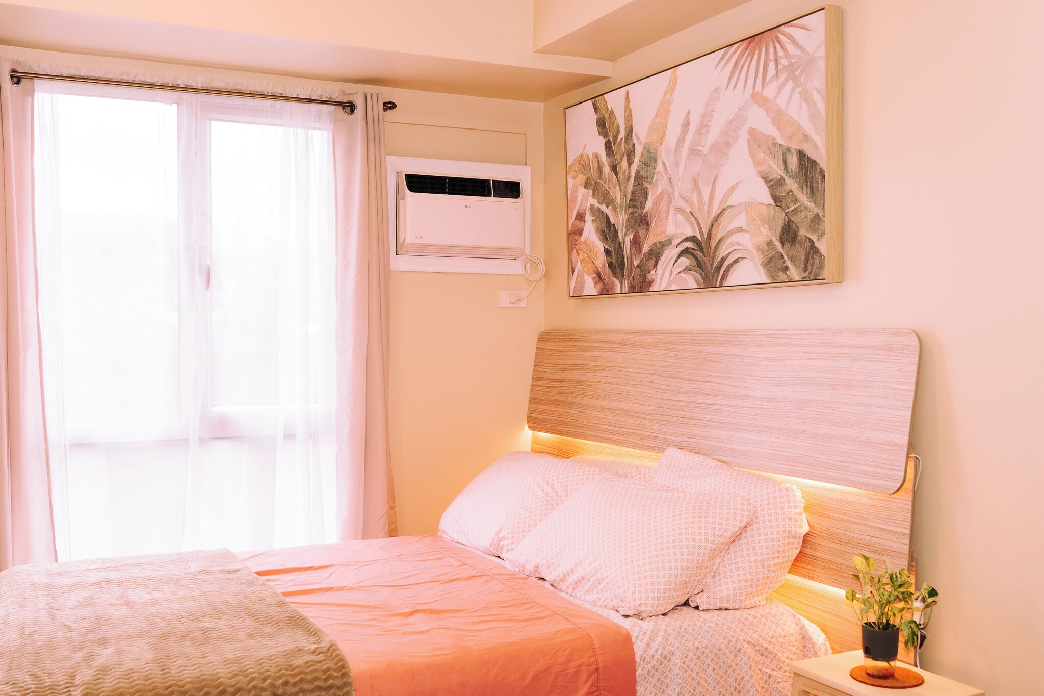 Ein Schlafzimmer mit einem Bett, einem Fenster mit Vorhängen, einer Klimaanlage und einer Wandpflanze.