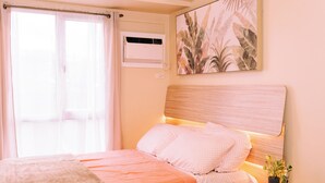 A bedroom with a bed, a window with curtains, an air conditioning unit, and a wall-mounted plant. - Designer Inspired Cozy Abode in the Heart of Cebu City (Cebu City)